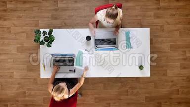 两位女士坐在桌子旁，一边工作，一边专注于工作过程，一边使用笔记本电脑
